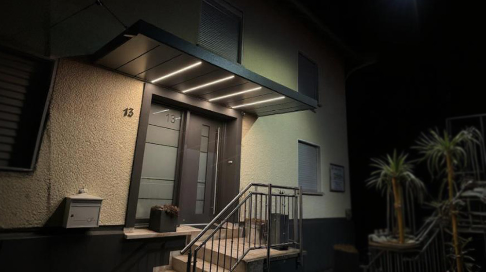 Moderne Haustür mit LED-Beleuchtung und Vordach bei Nacht