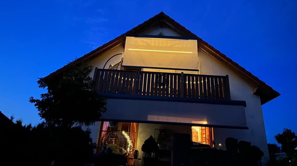 Beleuchtete Markise bei Nacht an einem Haus mit Balkon