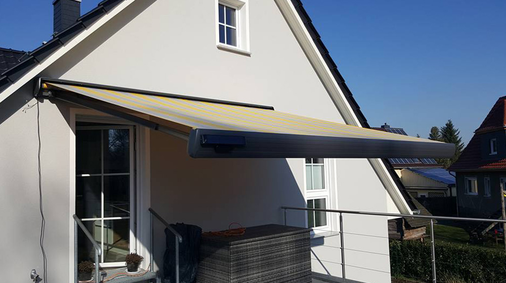 Moderne Gelenkarmmarkise auf Balkon – geschlossenes Gehäuse mit integriertem Volant