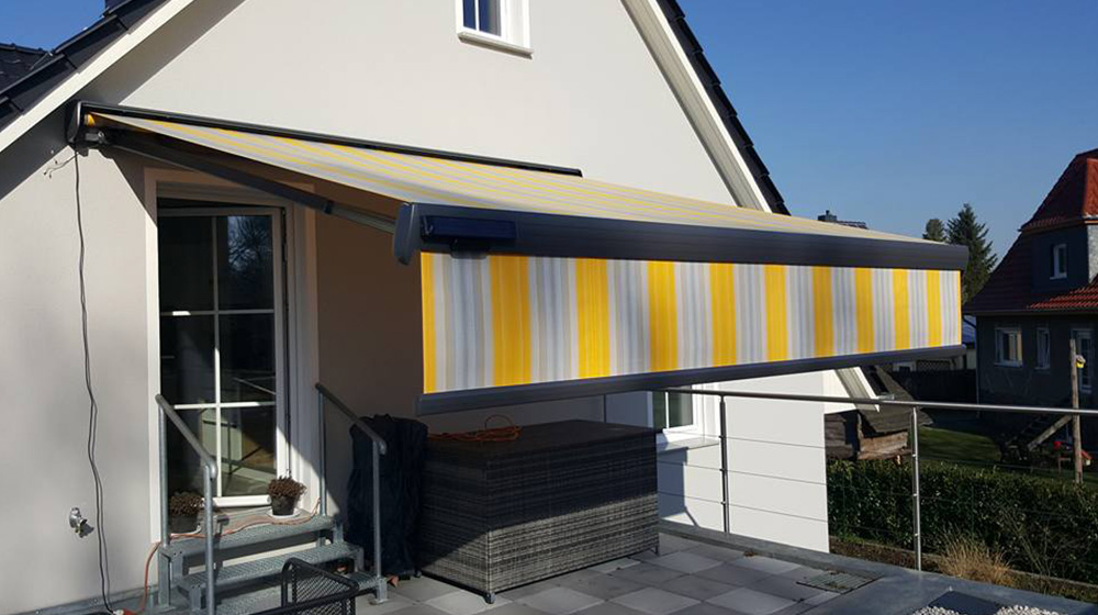 Markise mit gelb-grau gestreiftem Tuch und Volant – eleganter Schutz auf dem Balkon