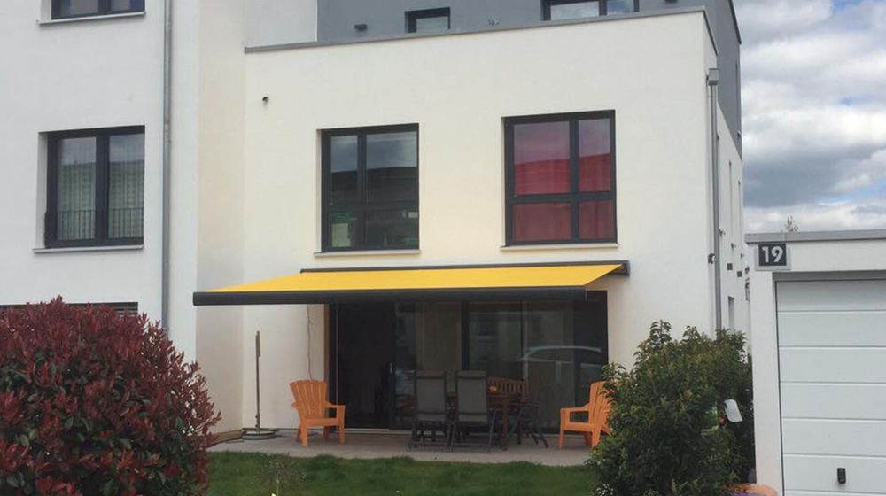 Ausgefahrene gelbe Gelenkarmmarkise über Terrasse eines Stadthauses