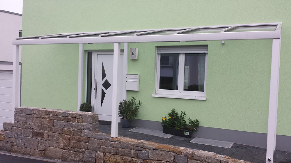 Moderne Haustür mit Glasvordach an grünem Haus