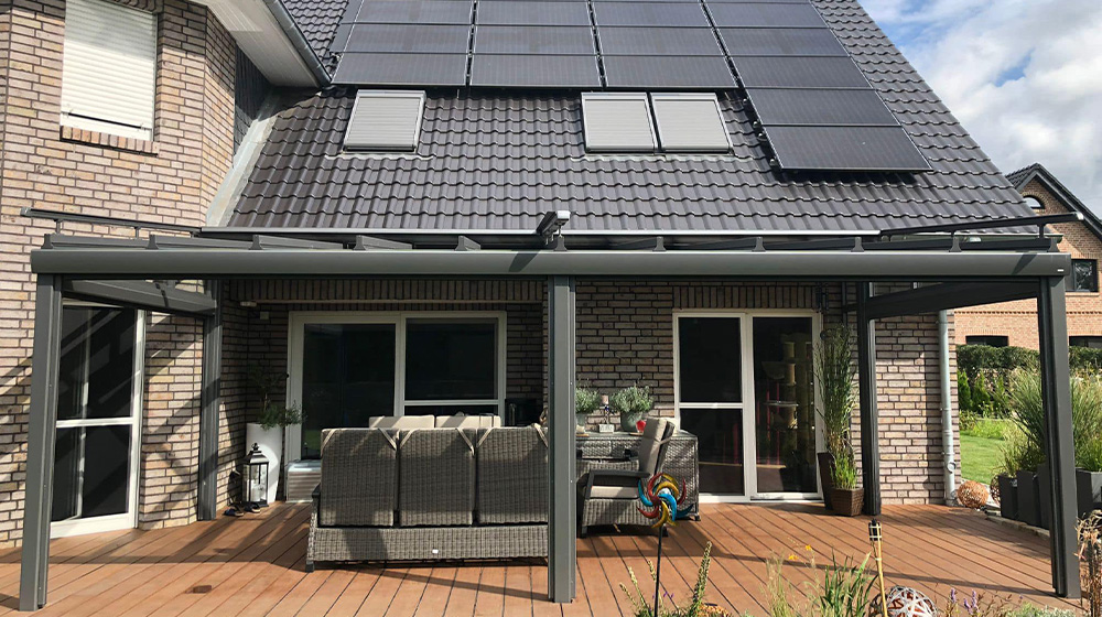 Alu-Terrassendach auf Holzterrasse mit gemütlichem Sitzbereich und Solarpanels am Haus