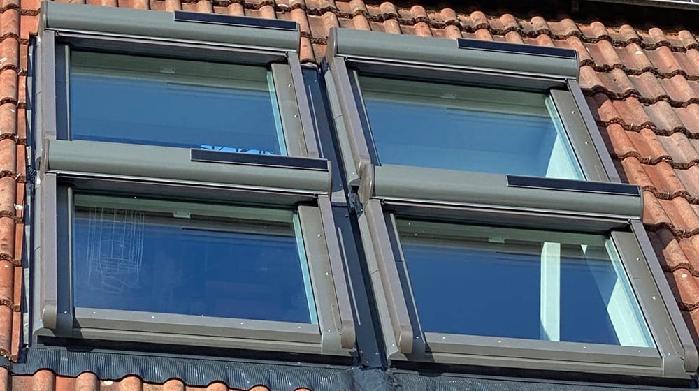 Vier moderne Dachfenster mit Rolläden auf einem Ziegeldach – stilvolle Lichtlösung