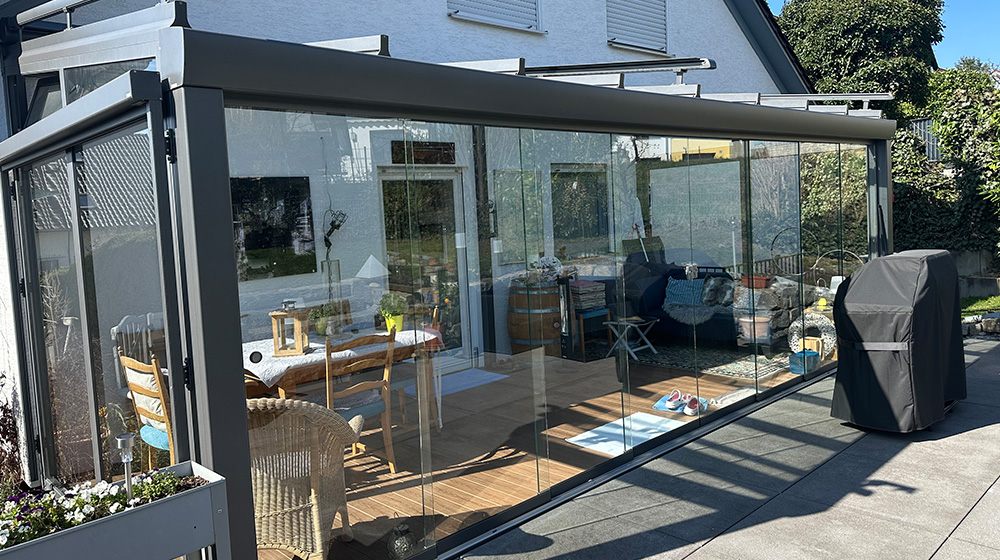 Terrassendach mit Glaswänden und gemütlicher Einrichtung – geschützter Wohnraum im Freien