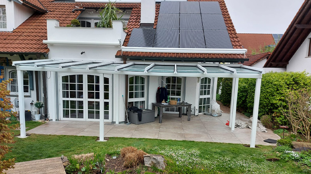 Terrassendach aus Aluminium und Glas an einem Haus mit Solarpanels auf dem Dach